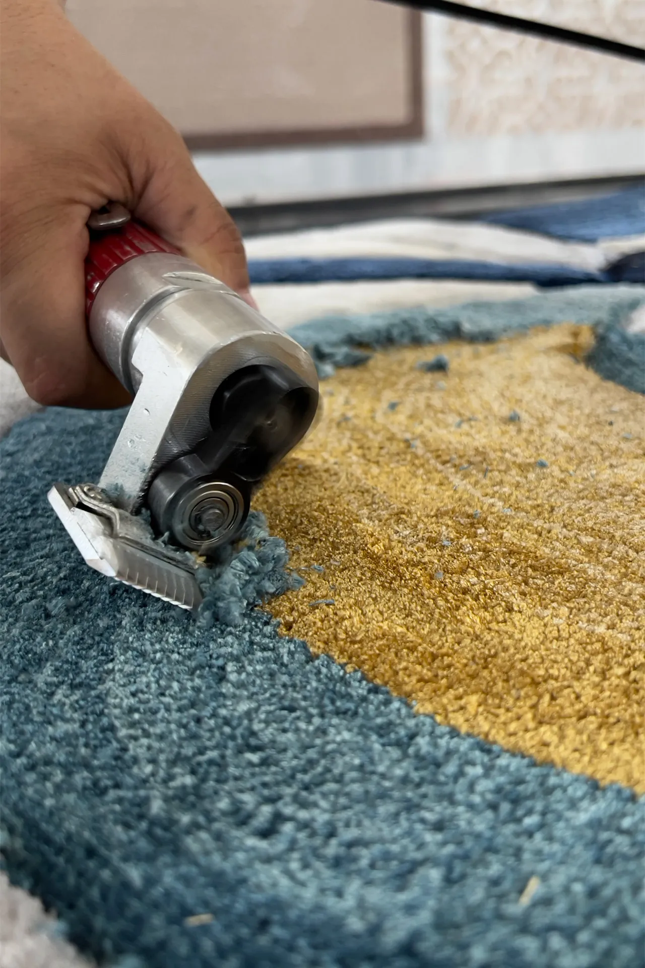 Close-up of a hand using a tufting gun to create a blue and yellow handmade rug.