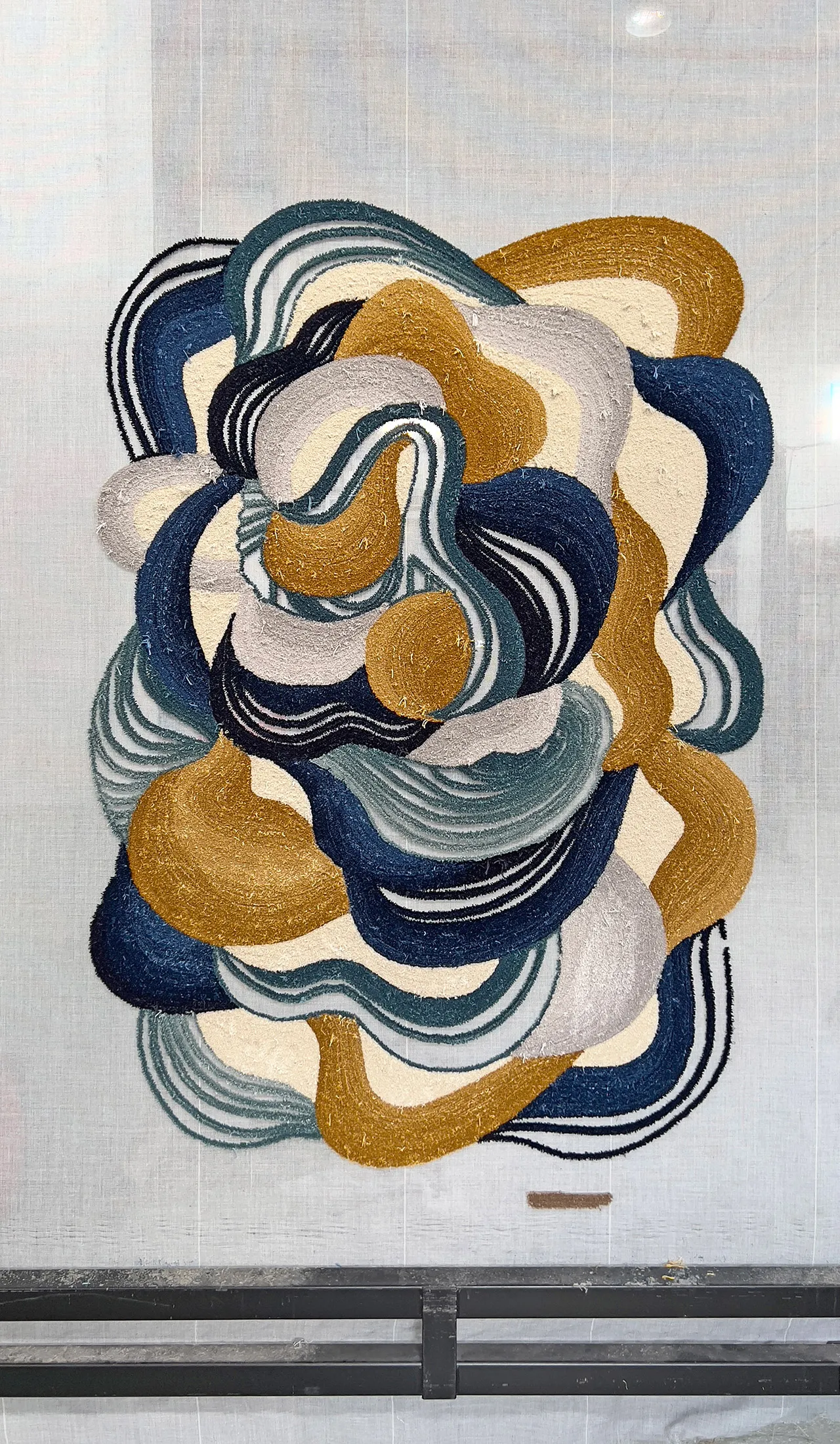 Abstract carpet hanging with intertwined flowing shapes in gold, navy, cream, black 