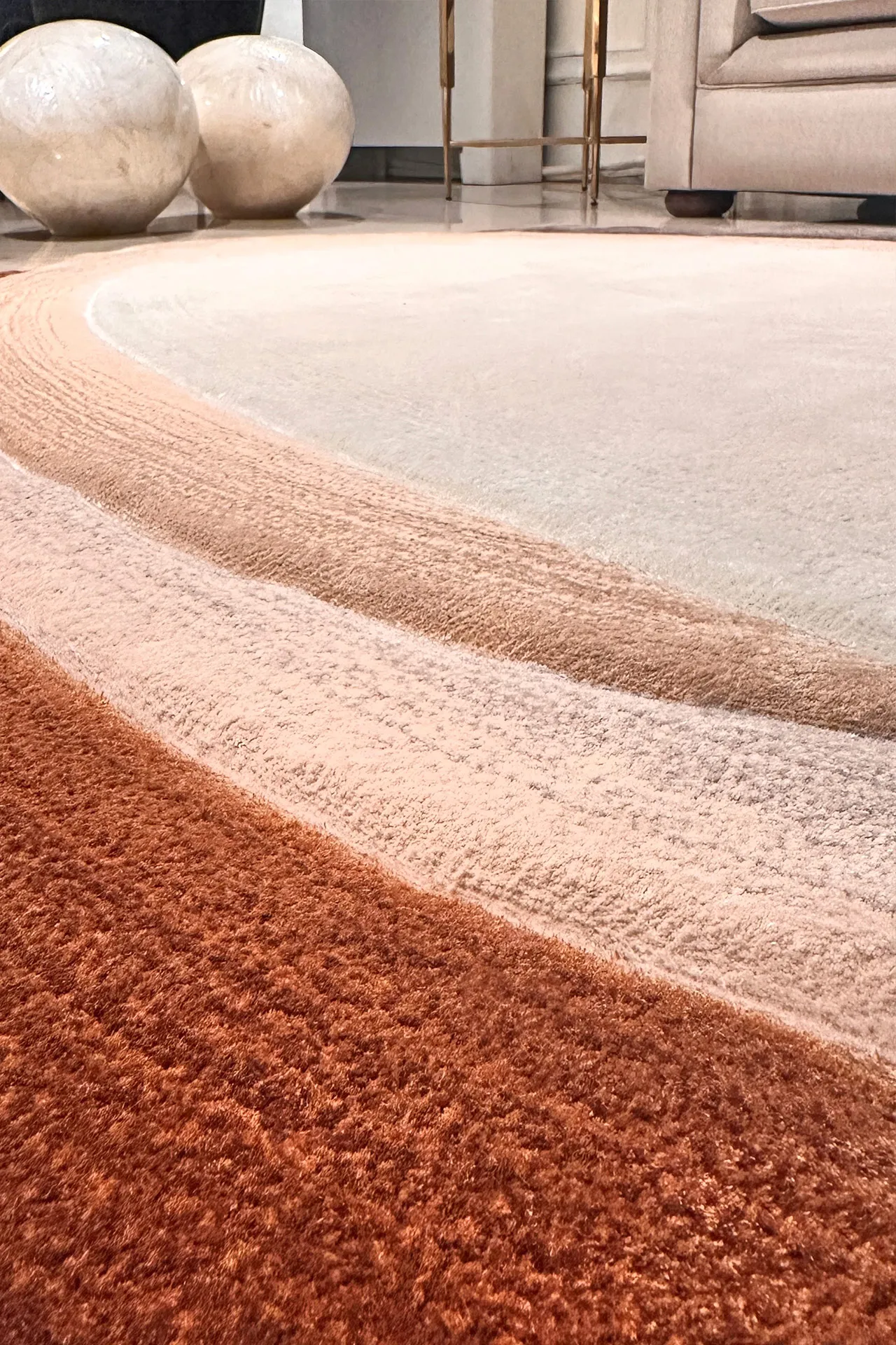 Close-up of a round, multi-toned rug with concentric textured rings in shades of rust, peach, and beige in a living room.